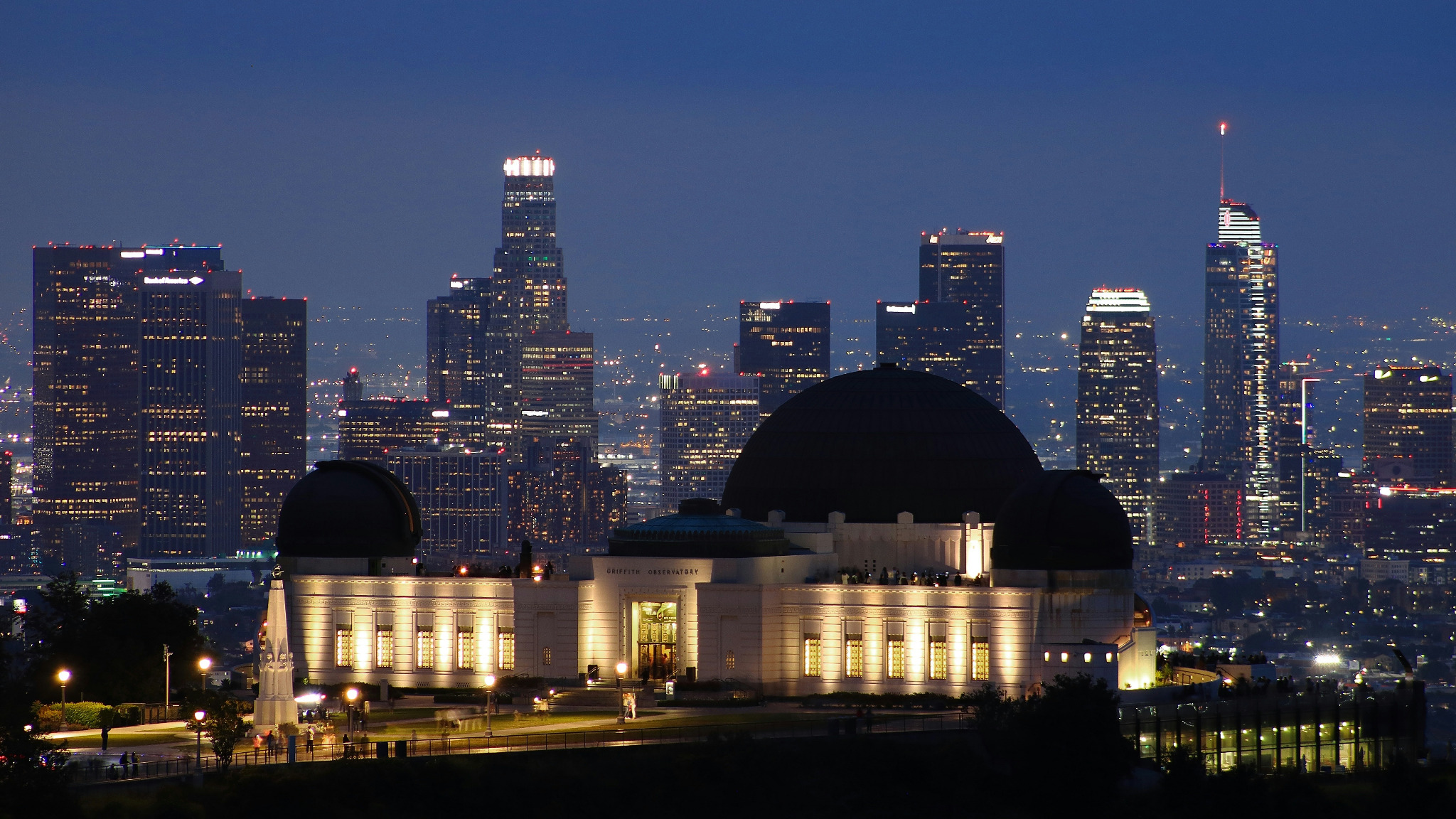 Griffith Observatory illuminated at night with the Downtown Los Angeles skyline behind it